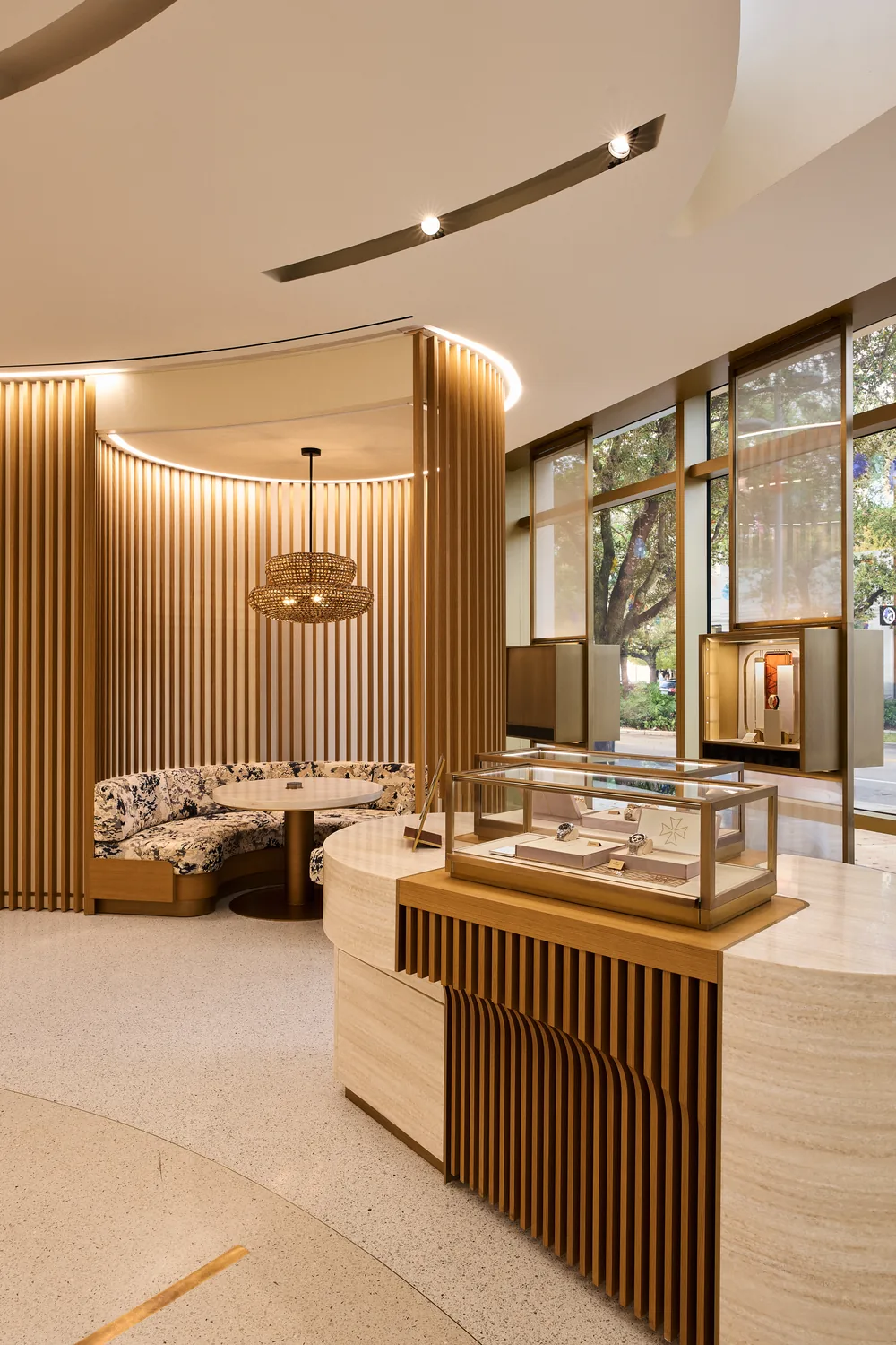 A watch boutique with a slatted timber seating alcove and a travertine counter carrying a lit glass vitrine.