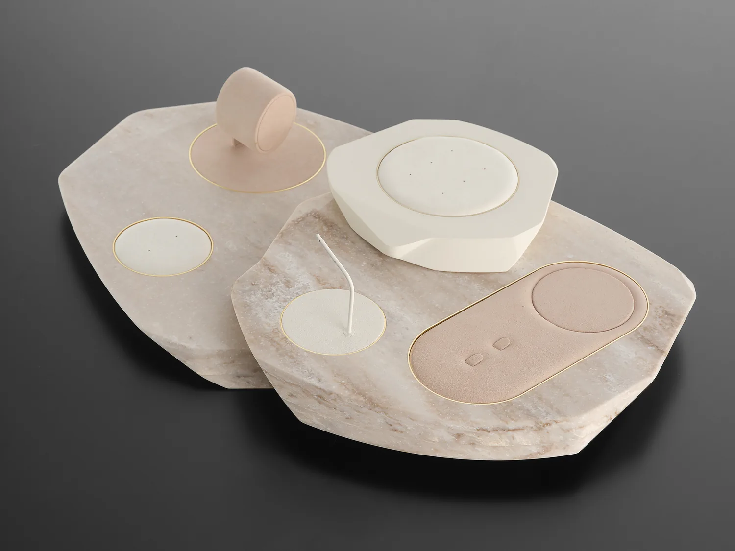 Pale stone presentation trays with a ring stand and pendant busts, arranged on grey.