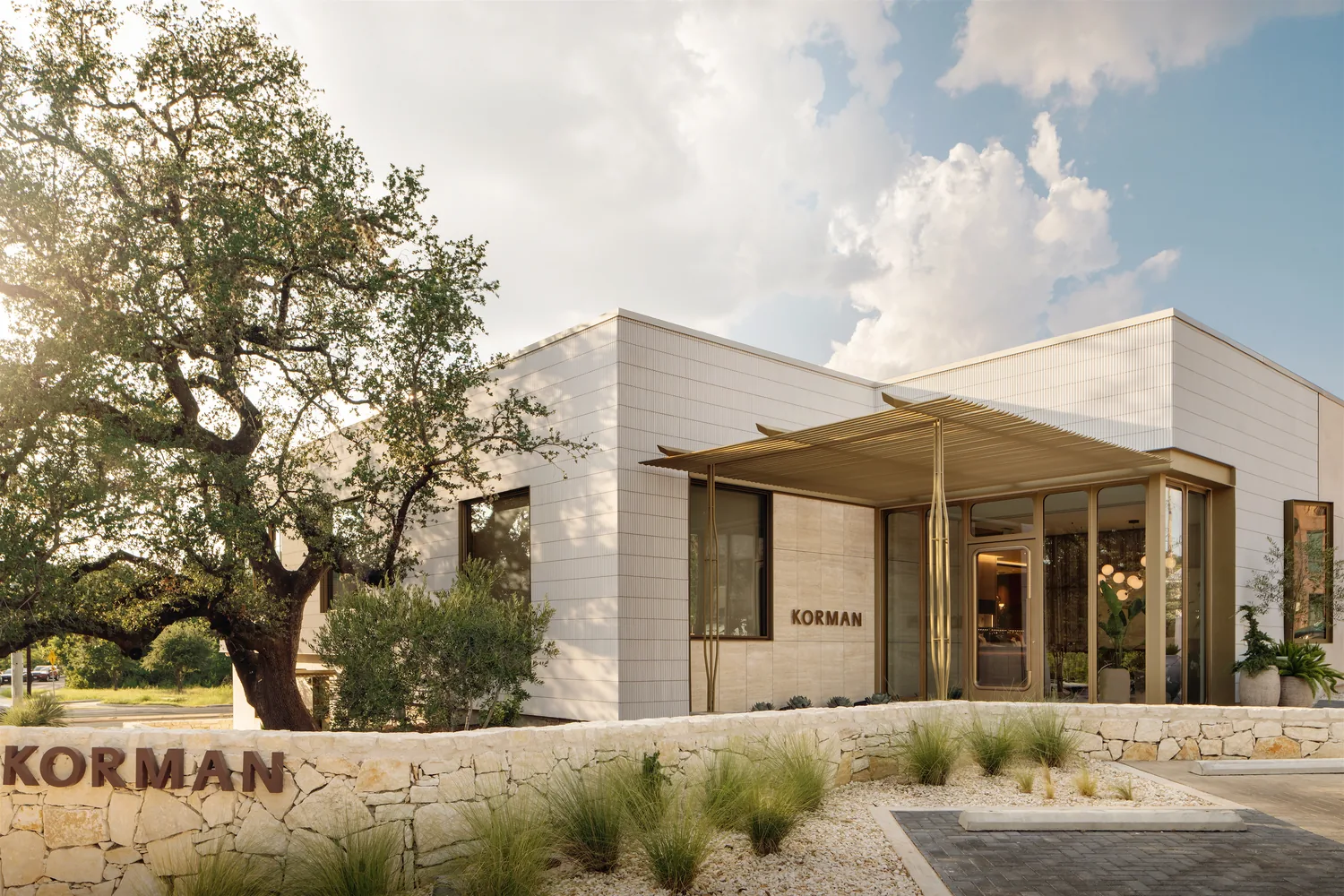 The Korman standalone boutique, a white building with a timber entrance canopy beneath a mature oak.